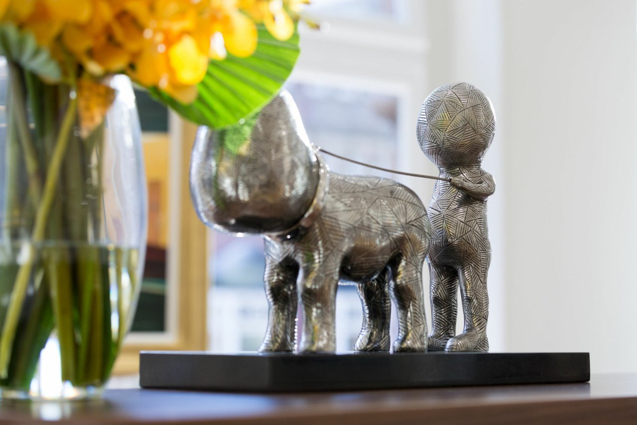  Walkies  by Billy Connolly, stainless steel sculpture of a man walking dog, £6,950  Pictured with yellow flowers  